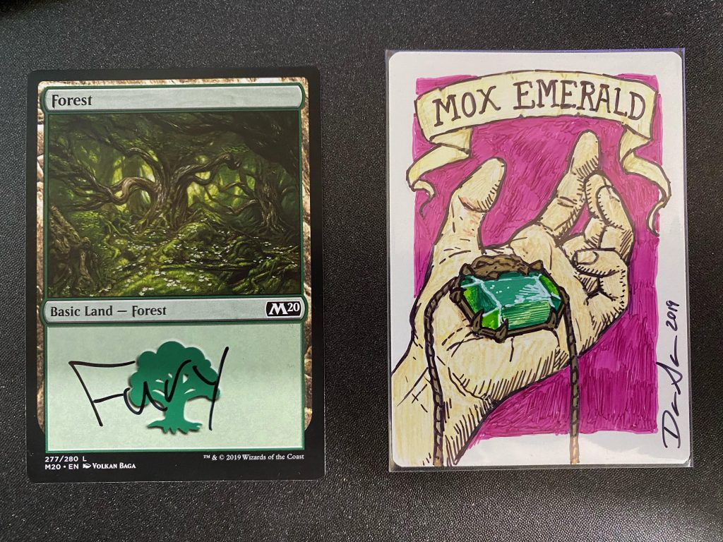 a basic Forest with the word Fury written in permanent marker and a custom color artwork of a Mox Emerald by Dan Scott